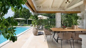 An outdoor pool area with a wooden table and chairs, surrounded by stone pillars and greenery. - Villa for 8 persons, pool, tennis court, outdoor fitness (Ladići)