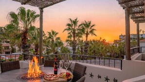 A terrace with a fire feature, dining table, wicker chairs, and a sunset view. - Charming Cabo Villa w/ Heated Pool, Hot Tub, Firepit, Palapa & Ocean Views (Cabo San Lucas)