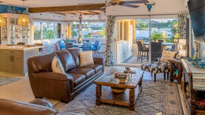 A spacious living room with a brown leather sofa, a wooden coffee table, and a dining area with patterned chairs. - Charming Cabo Villa w/ Heated Pool, Hot Tub, Firepit, Palapa & Ocean Views (Cabo San Lucas)