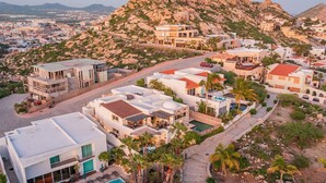 A coastal residential area with modern houses, a swimming pool, and a mountainous backdrop. - Charming Cabo Villa w/ Heated Pool, Hot Tub, Firepit, Palapa & Ocean Views (Cabo San Lucas)