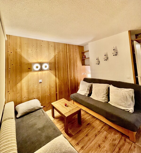 Un salon chaleureux avec un mur d’accent en bois, un canapé gris foncé et une petite table basse en bois.