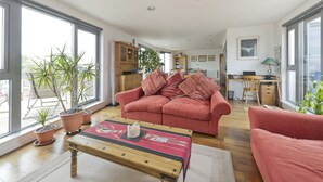 A spacious living area with a red sofa, a wooden coffee table, and potted plants. - Putney Rooftops - Two Bedroom Apartment, Sleeps 4 (London)