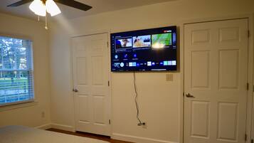 A bedroom with a bed, a ceiling fan, a TV mounted on the wall, and a window with blinds.