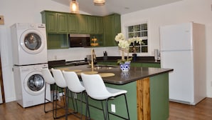 Cocina con gabinetes verdes, lavadora, refrigerador y una zona con taburetes de bar.