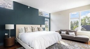 Relax in this serene bedroom with a large bed against a dark accent wall, complemented by a sofa and natural light from the window.