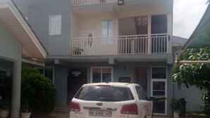 A multi-story building with a white car parked in front. - Impeccable Comfortable One Bed Apartment in Accra (Ogbodjo)
