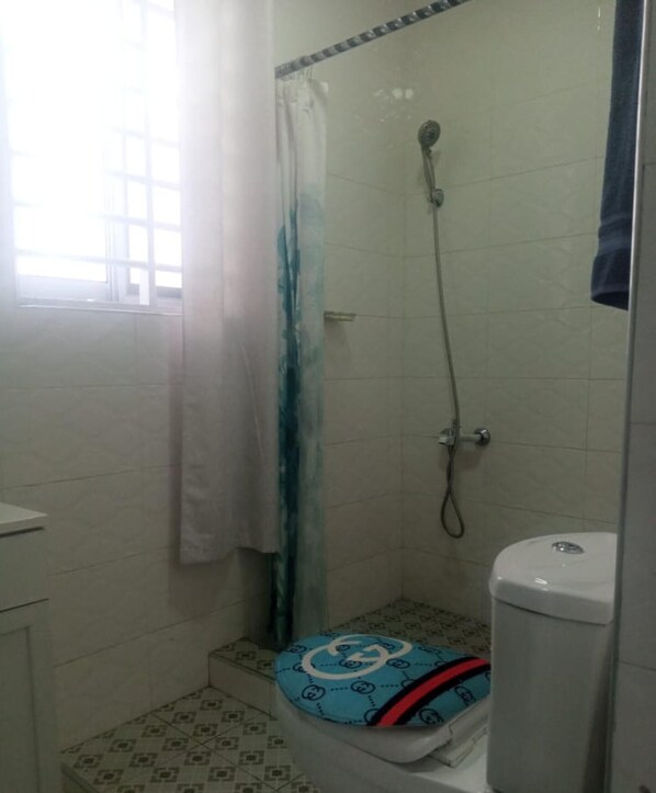 A small bathroom with a shower, toilet, and a patterned floor. - Impeccable Comfortable One Bed Apartment in Accra (Ogbodjo)