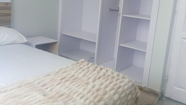 A bedroom with a bed, a white wardrobe, and a white blanket. - Impeccable Comfortable One Bed Apartment in Accra (Ogbodjo)