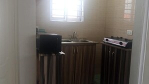 A compact kitchen with wooden cabinets, a sink, and a stove. - Impeccable Comfortable One Bed Apartment in Accra (Ogbodjo)