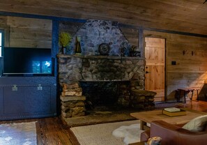 A cozy living room with a stone fireplace, wooden walls, a flat-screen TV, and a wooden door.