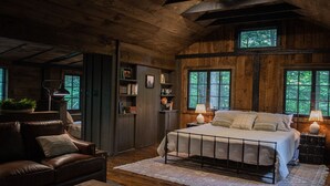 Une chambre confortable dans un chalet en bois, avec un grand lit, un canapé en cuir, une bibliothèque et une fenêtre donnant sur la forêt.