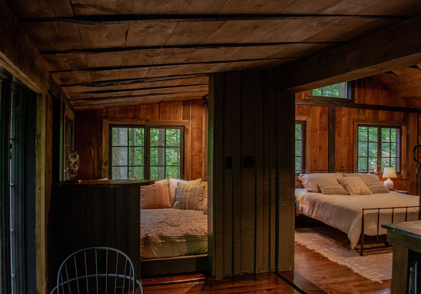 A rustic cabin with two bedrooms, wooden floors, and large windows.