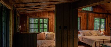 A rustic cabin with two bedrooms, wooden floors, and large windows.