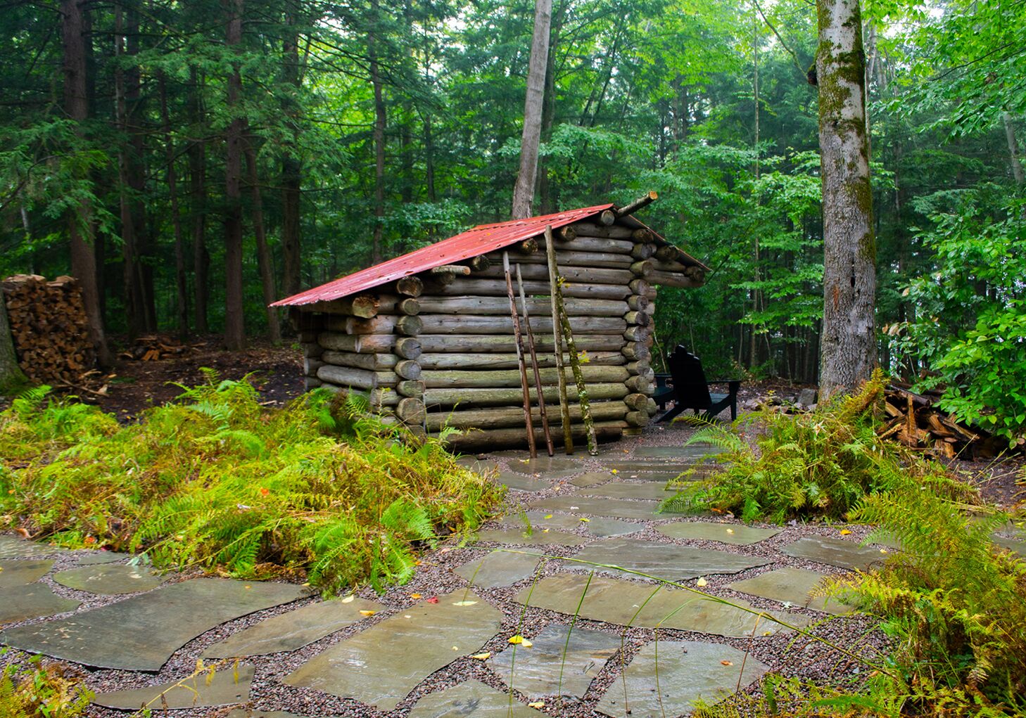 A log cabin with a red roof, surrounded by a forest.