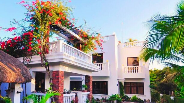 A two-story building with a balcony, surrounded by lush greenery and a well-maintained garden. - Bernardos Lantia Hotel (Basco)