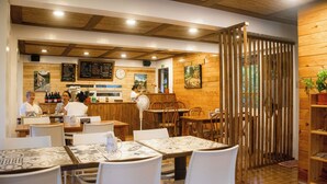 A restaurant with wooden interior, tables with white chairs, a counter with a menu, and a clock on the wall. - Bernardos Lantia Hotel (Basco)