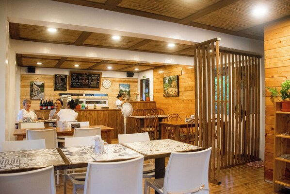 Un restaurante con interior de madera, mesas con sillas blancas, una barra con menú y un reloj en la pared.