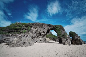 Formación rocosa natural con una abertura similar a una cueva en una playa arenosa.