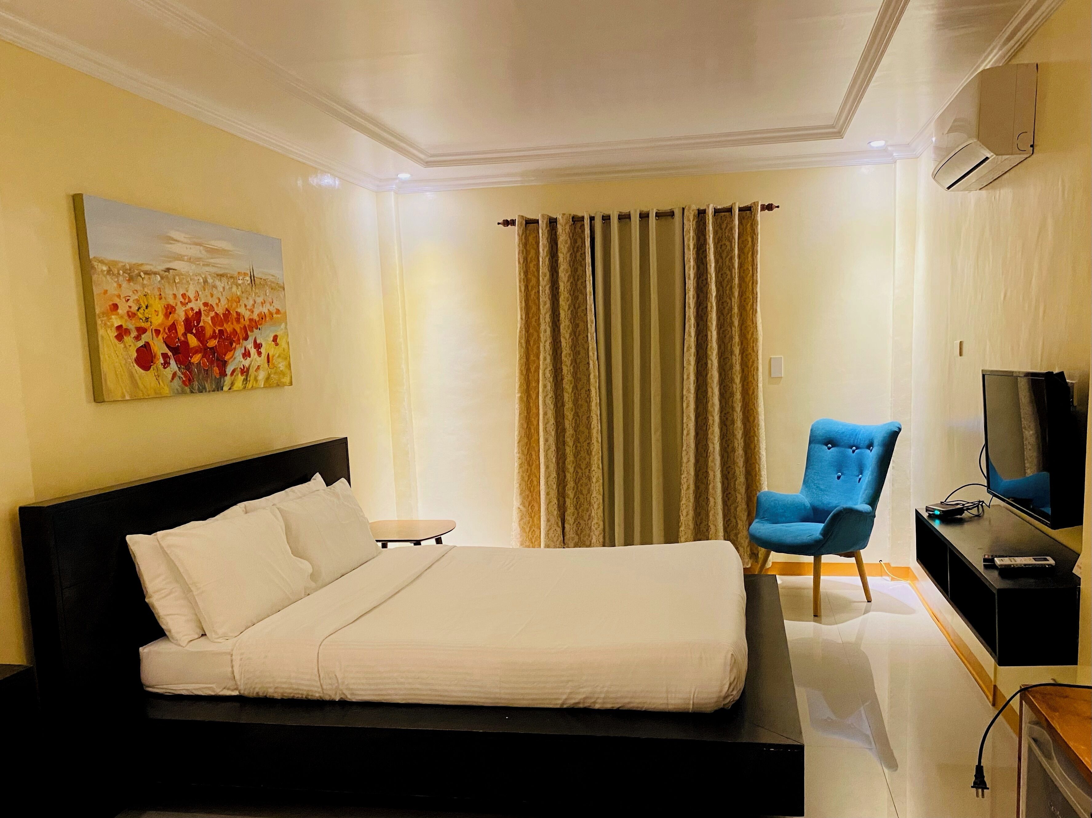 A hotel room with a bed, a chair, a TV, and an air conditioning unit.