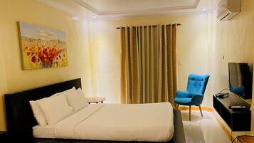 A hotel room with a bed, a chair, a TV, and an air conditioning unit.