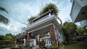 A two-story house with a balcony, surrounded by lush greenery and a well-maintained garden. - Bernardos Lantia Hotel (Basco)