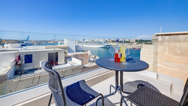 En balkon med et bord og stole, der giver udsigt over en lystbådehavn med både og et krydstogtskib.