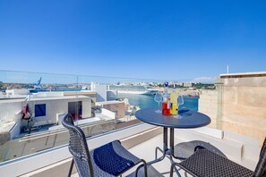 A balcony with a table and chairs, overlooking a marina with boats and a cruise ship. - Traditional Maltese Townhouse wt Terrace and Pool (Senglea)