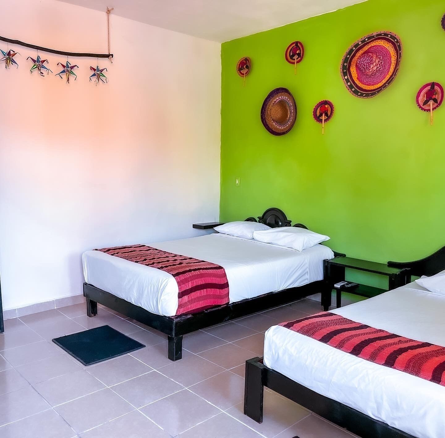 A hotel room with two beds, a green accent wall, and decorative wall hangings.