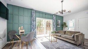 Una sala de estar con un sofá, dos sillones, una mesa de centro, un televisor y un amplio ventanal con cortinas.
