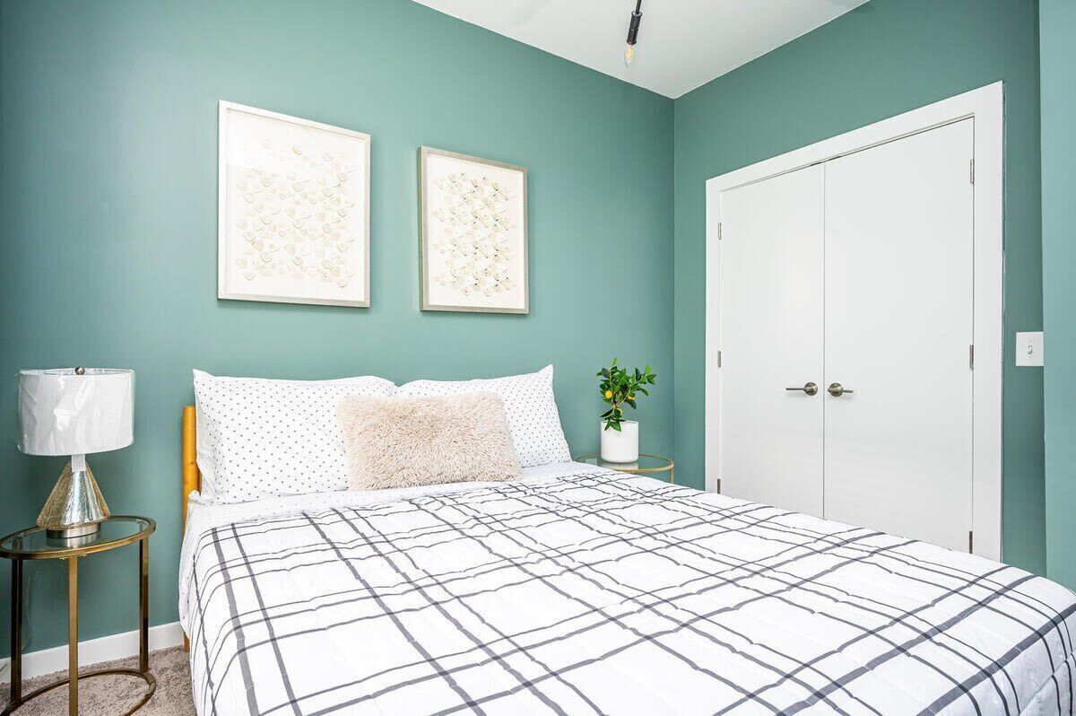 Une chambre à coucher avec un lit, deux tableaux encadrés, une table de chevet, une lampe, une plante en pot et une armoire blanche.