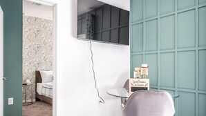 Una habitación moderna con una cama, una mesa redonda de vidrio, una silla, un televisor montado en la pared y un cartel de bienvenida.
