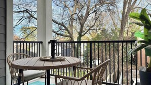 A covered outdoor area with a round table and wicker chairs, a potted plant, and a view of trees and a brick wall. - Stylish 2B2B Apartment in Atlanta's Old Fourth Ward (Atlanta)