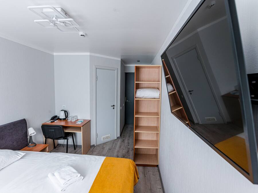 A hotel room with a bed, a desk, a chair, a wardrobe, and a television.