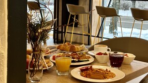 A breakfast table with various dishes, a vase with greenery, and a view of a snowy landscape through large windows.