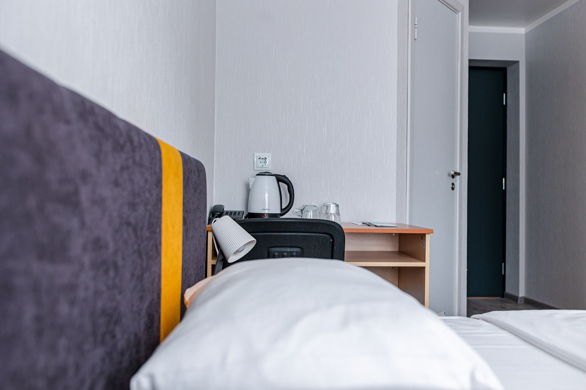A hotel room with a bed, a desk with a kettle, a phone, and a coffee maker.