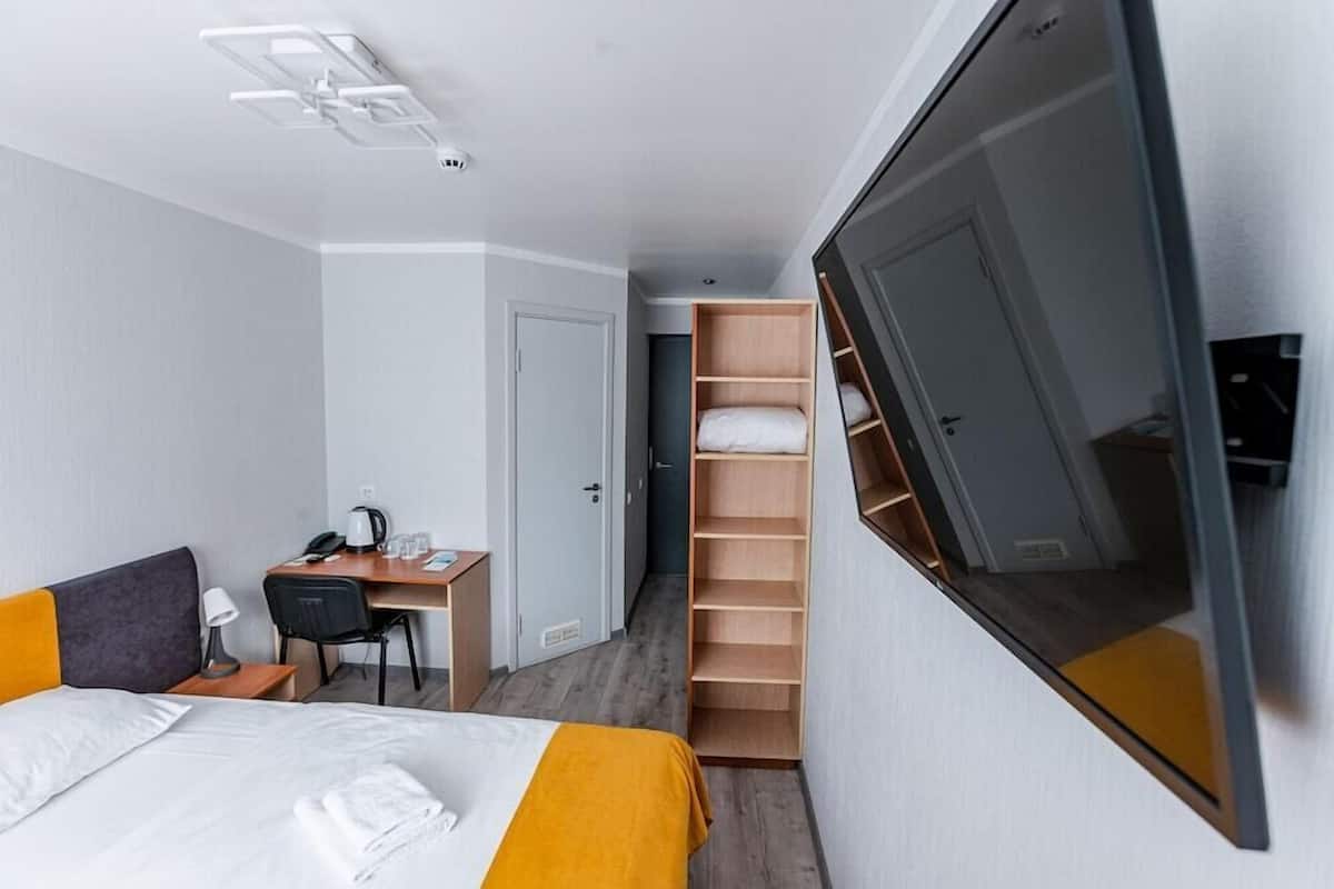 A hotel room with a bed, desk, chair, and a wardrobe with shelves.