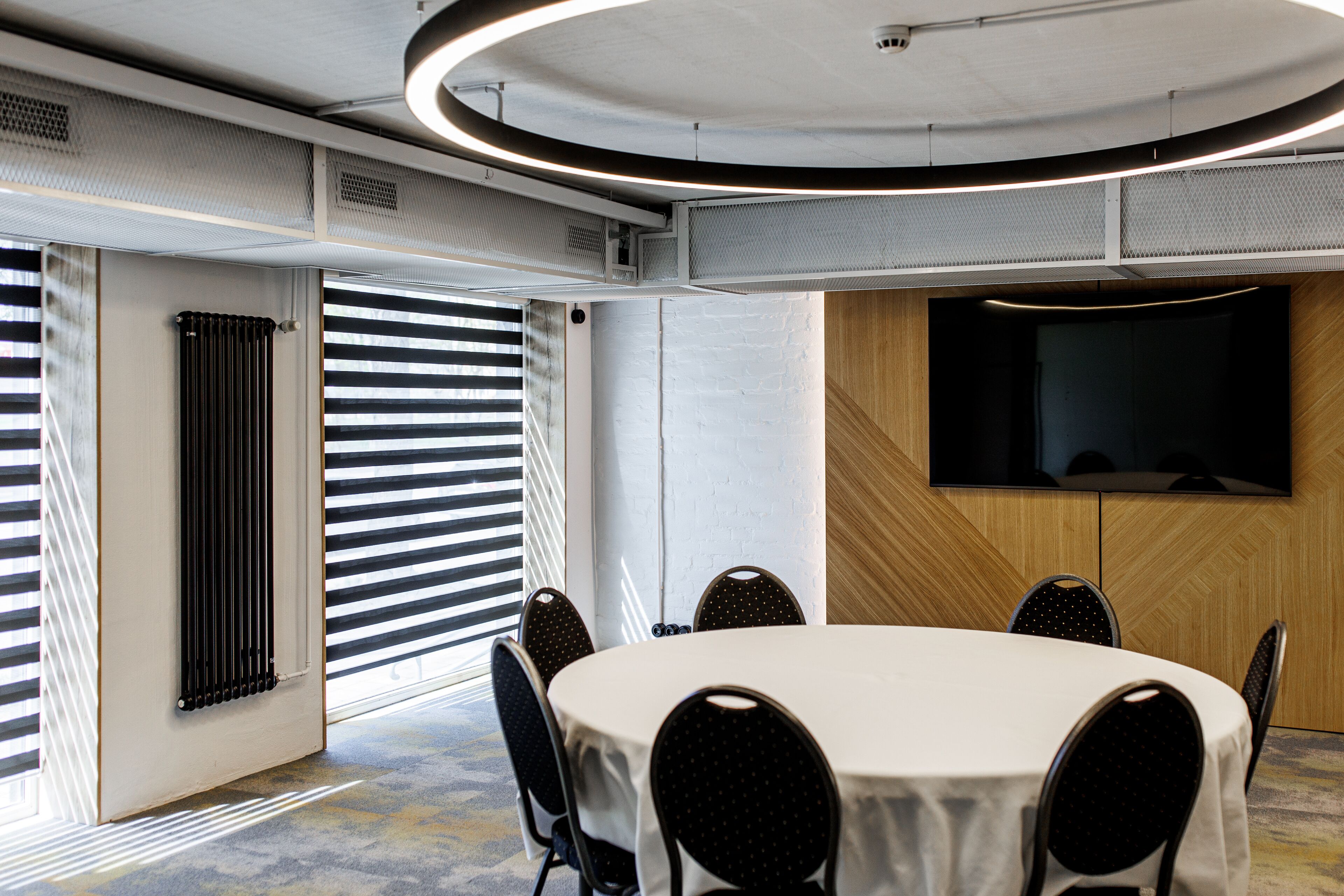 A conference room with a round table, black chairs, a large flat-screen TV, and a radiator.