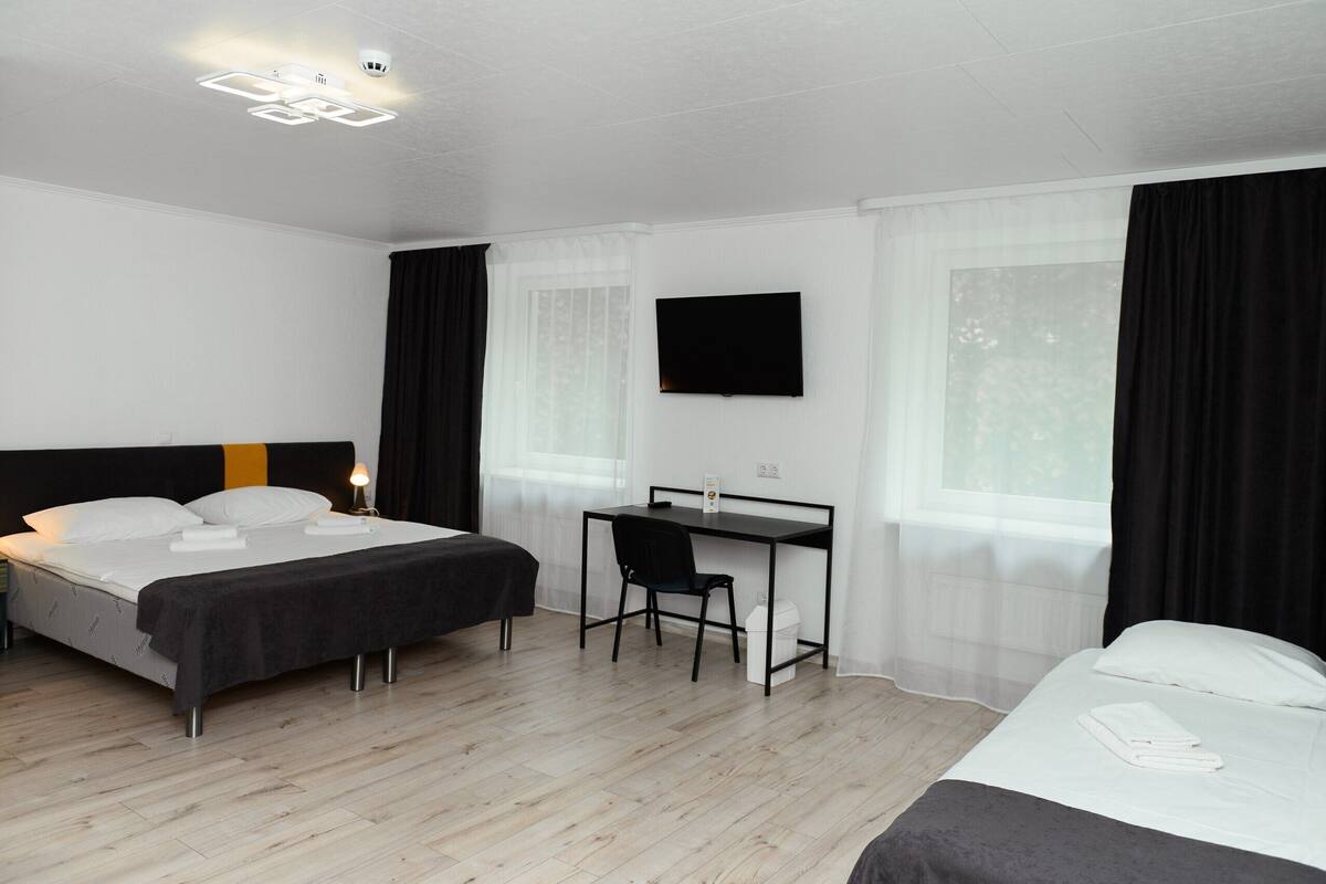 A hotel room with a bed, a desk, a chair, a TV, and a window with curtains.