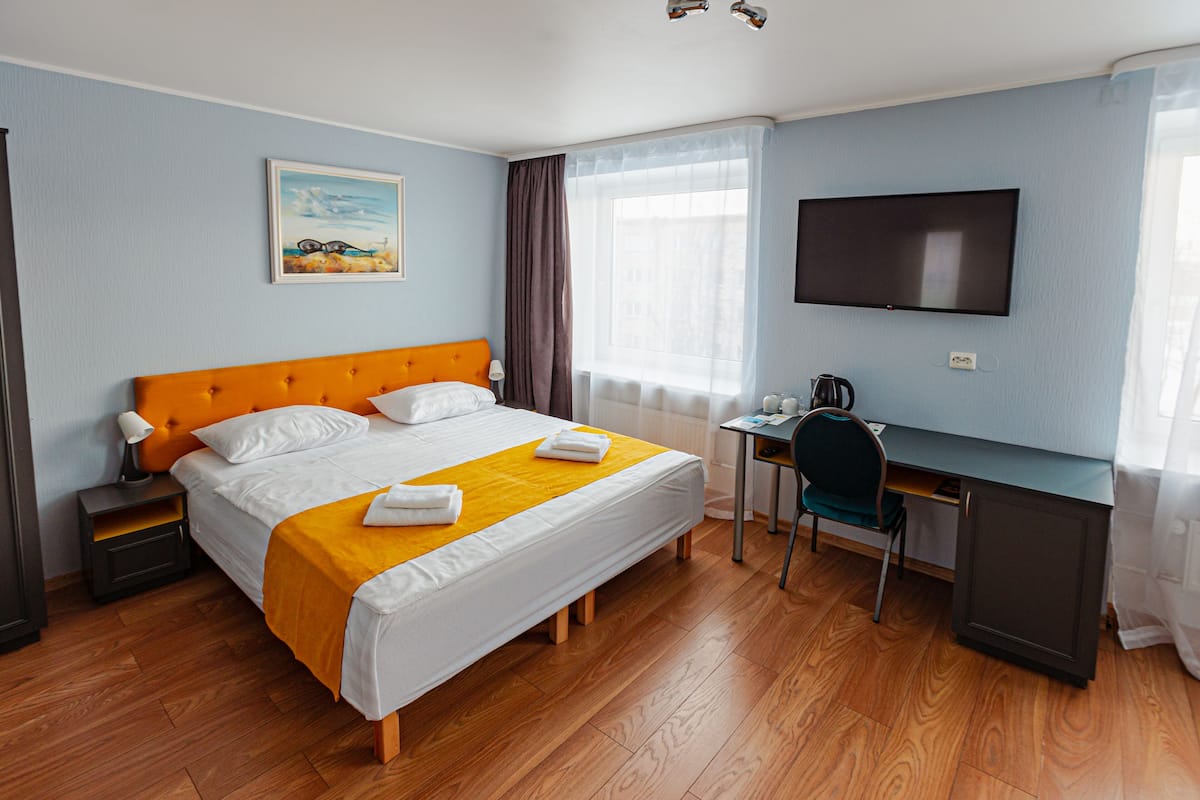 A hotel room with a bed, a desk, a chair, a television, and a window with curtains.