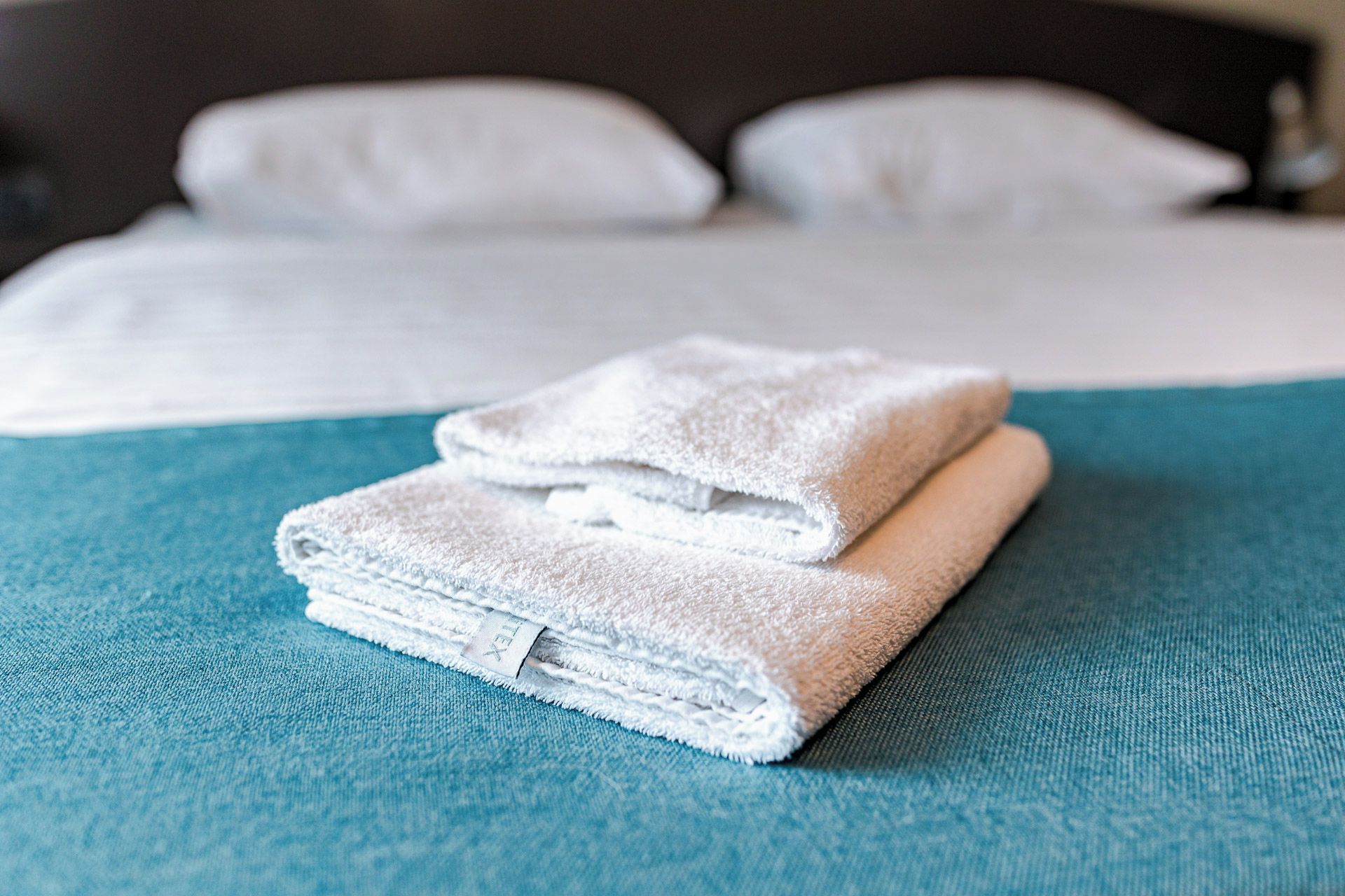Una cama bien hecha con sábanas blancas y una colcha color aguamarina.