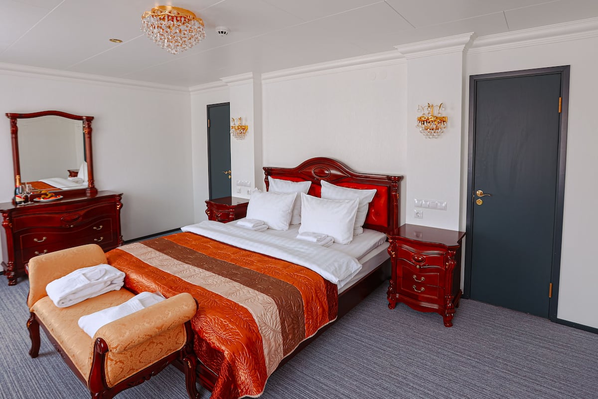 A neatly arranged hotel room with a large bed, a wooden dresser, a vanity with a mirror, and a door.