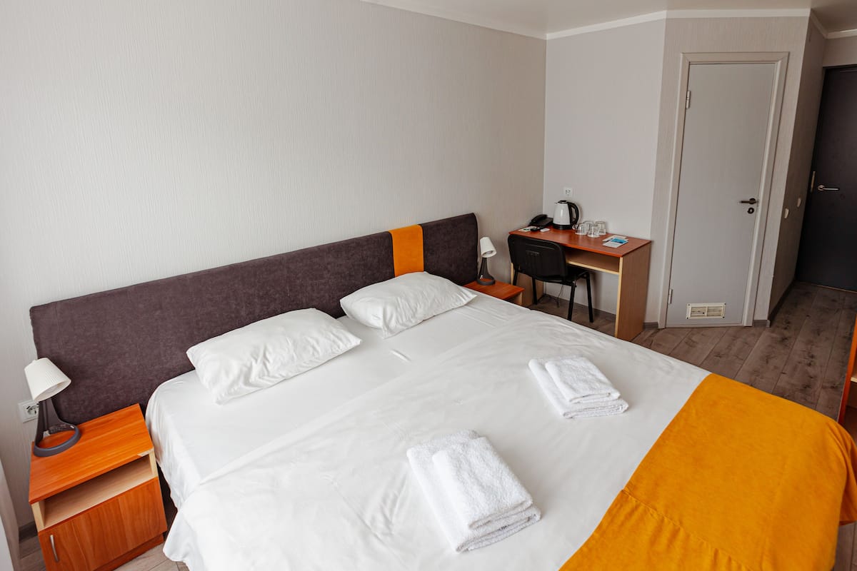 A hotel room with a bed, a desk, a chair, and a door.