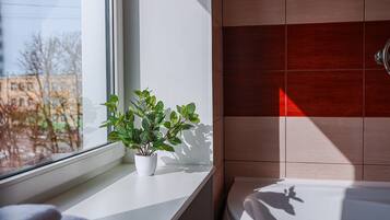 Un baño con ventana, planta en maceta y bañera.