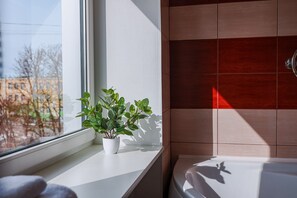 A bathroom with a window, a potted plant, and a bathtub.