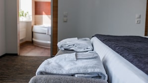 A hotel room with a neatly made bed, a bathroom visible through an open door, and a small table with folded towels.