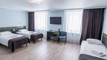 Habitación de hotel con dos camas individuales, un escritorio con silla, un televisor de pantalla plana y un ventanal con cortinas.