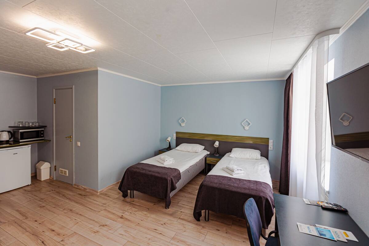 A hotel room with two single beds, a desk with a chair, a microwave, and a small kitchenette.