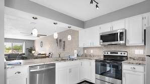 Una cocina moderna con armarios blancos, electrodomésticos de acero inoxidable, microondas, horno y lavavajillas.