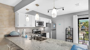 Una cocina moderna con armarios blancos, encimera de granito, electrodomésticos de acero inoxidable e iluminación colgante.