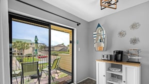 Una habitación con puerta de vidrio corredera que da a un balcón, un armario blanco con estantes y decoración en la pared.